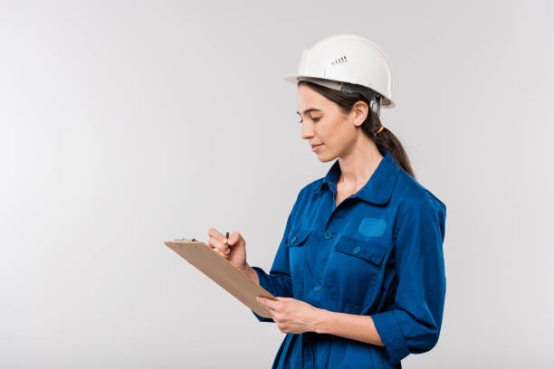 青い作業服と安全ヘルメットの若い成功した女性エンジニアはノートを作る - construction young adult architect women ストックフォトと画像