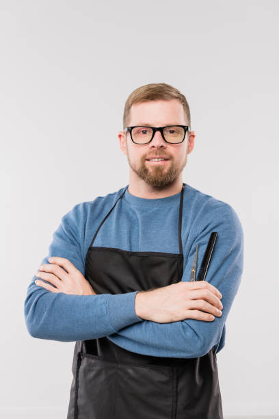 istock Young bearded hairdresser in apron and blue pullover waiting for clients 1192515128