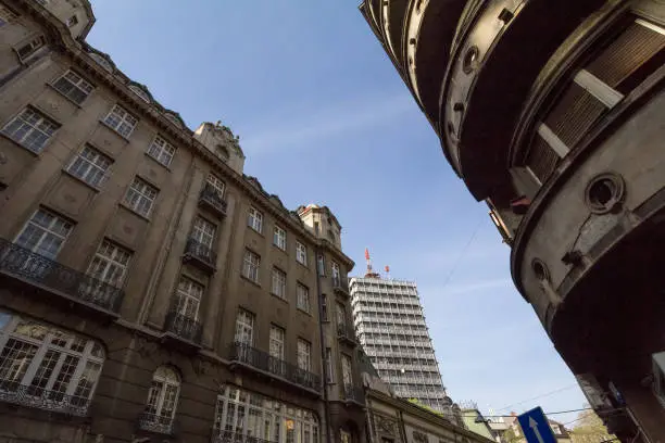 Photo of Old residential buildings made of concrete and a 70s high rise steel skyscraper in the city center of Belgrade, the capital city of Serbia, during a sunny afternoon.