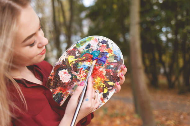 istock Young painter mixes paints on a palette that she holds in her hands. 1192527927