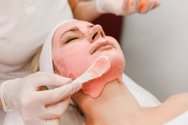 doctor esteticista aplica máscara anti-envejecimiento a la cara de la mujer. las niñas se encuentran en un procedimiento de cosmetología. primer plano de la mascarilla facial - mud wellbeing spa treatment beautician fotografías e imágenes de stock