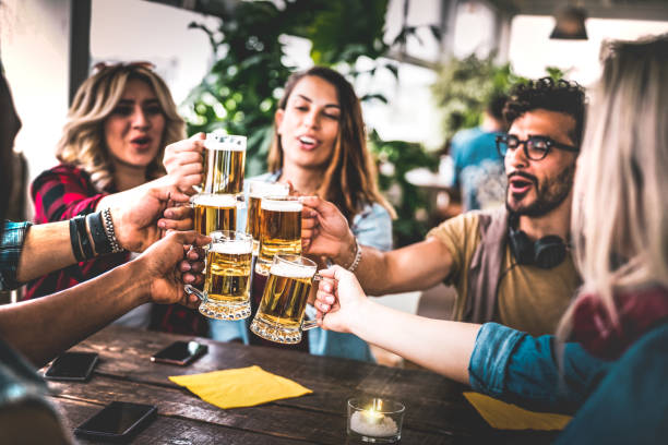 friends toasting beer at brewery bar indoor at rooftop party - friendship concept with young people having fun together drinking at happy hour promotion - focus on glasses - warm vignetting filter - beer pub women pint glass imagens e fotografias de stock