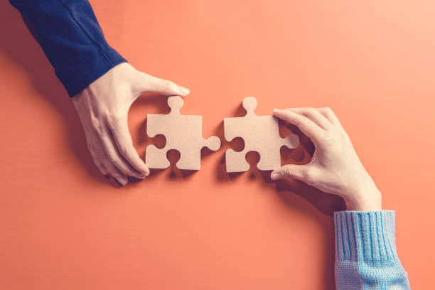 two hands holding jigsaw, concept for teamwork building a success. - partnership cooperation teamwork puzzle imagens e fotografias de stock