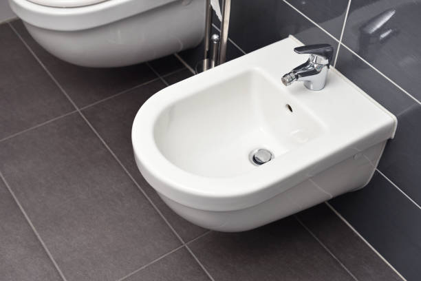 White bidet screwed to a gray tiled wall in the bathroom, close-up stock photo