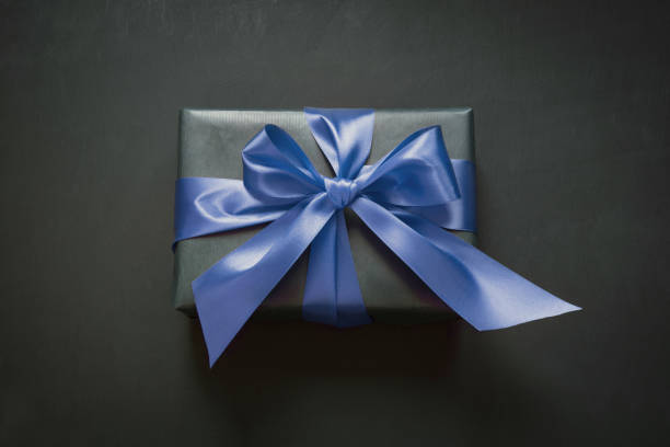 istock Gift box wrapped in black paper with classic blue ribbon on black surface. 1192545950