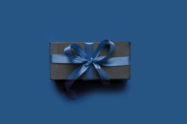 istock Black gift box wrapped with blue ribbon on classic blue surface. 1192545953