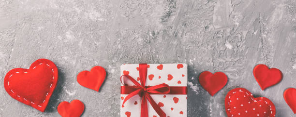 Valentine or other holiday handmade present in paper with red hearts and gifts box in holiday wrapper. Present box of gift on grey cement table top view with copy space, empty space for design. san valentín u otro regalo de vacaciones hecho a mano en papel con corazones rojos y caja de regalos en envoltorio de vacaciones. caja de regalo presente en la vista superior de la mesa de cemento gris con espacio de copia, espacio vacío para el diseño