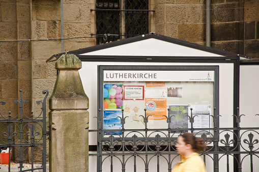 A pedestrian walking past a notice board outside a Lutherkirche in Dortmund-Hörde, Germany. Lutherkirche or Luther Church are common names for churches named after Martin Luther in German-speaking countries