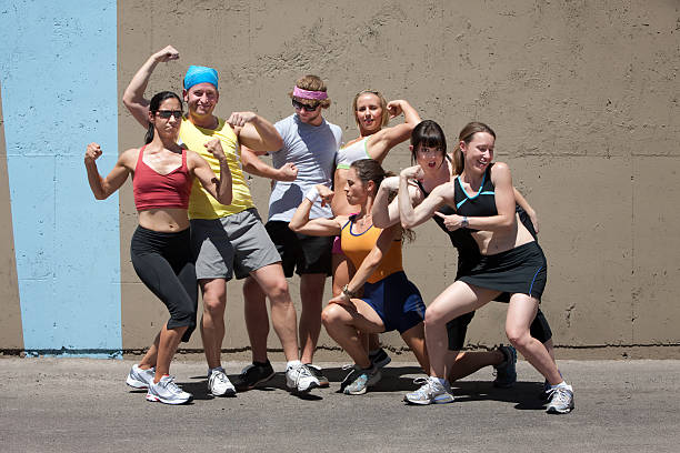 Multi ethnic team standing side by side on outdoor basketball court. They are wearing different type of sportswear. Caucasian woman in orange t-shirt is holding a basketball and bottle of water. They are all serious and focused.