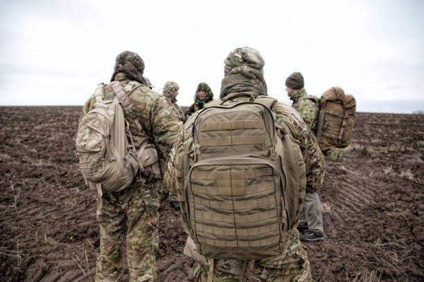 Army soldiers group on march in muddy field Army soldiers on march. Elite forces fighters group, commando tactical unit, reconnaissance team members in camouflage uniform, walking in line, carrying backpacks on muddy terrain militant groups photos stock pictures, royalty-free photos & images