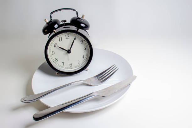 istock Losing weight. A fork, knife with a clock on a white plate on a white background 1192572615