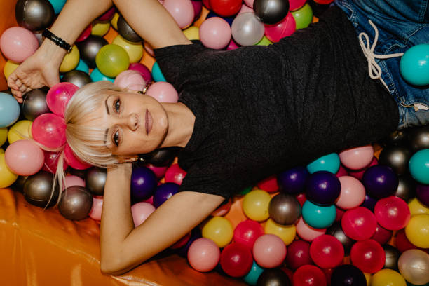 smiling young woman lying down in ball pool - ball pool imagens e fotografias de stock