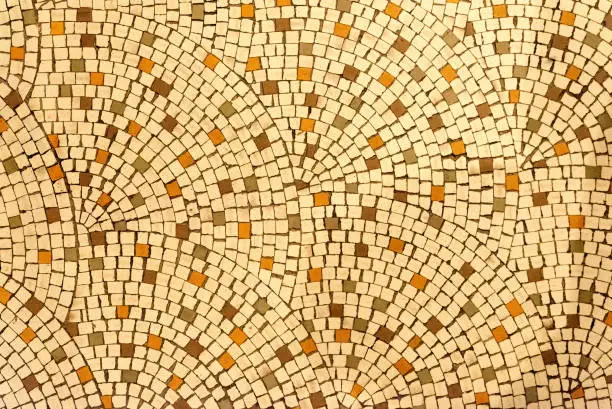 Looking straight down at a simple yellowish ceramic tile floor. It looks like the type of floor seen in a Roman or Greek villa. Tile exhibits a fan pattern.