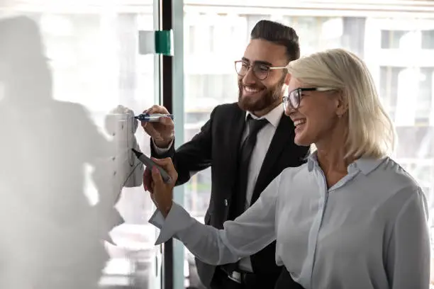 Photo of Smiling diverse colleagues brainstorm in office writing on bard