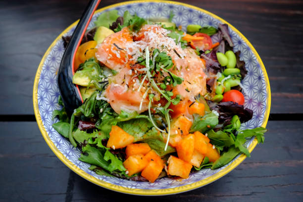 Healthy salmon avocado salad bowl Close up shot of healthy salad bowl with sliced raw salmon ,avocado, mango and leaf vegetables above dark wooden table seafood salad stock pictures, royalty-free photos & images