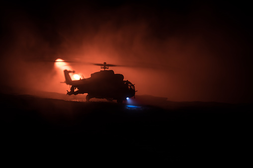 Silhouette of military helicopter ready to fly from conflict zone. Decorated night footage with helicopter starting in desert with foggy toned backlit. Selective focus. War concept