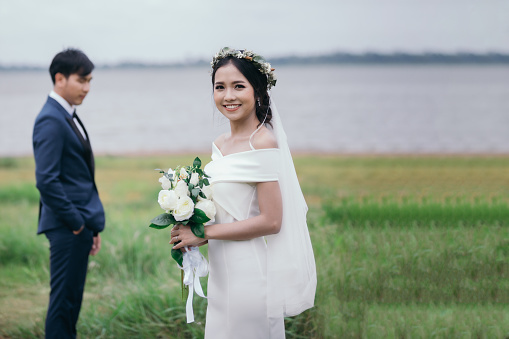 Wedding couple, Smiling bride holds a wedding bouquet in her hands and the groom is wearing a suit on background the green meadow.