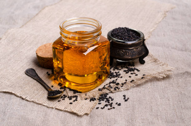 Glass jar with oil. Black sesame seeds. Textile background. Selective focus.