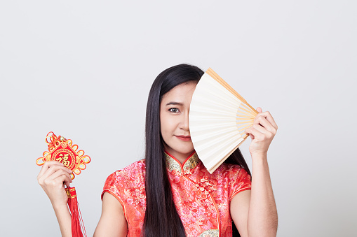 Young asia woman with cheongsam holding a fan with chinese traditional ornament means good luck and smiling at the camera, good fortune.the \