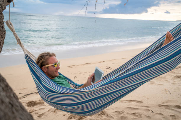 istock Digital nomad- Man relaxing on hammock at sunset by the beach with digital tablet 1192609990