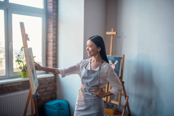 istock Joyful nice woman standing in front her painting 1192610658