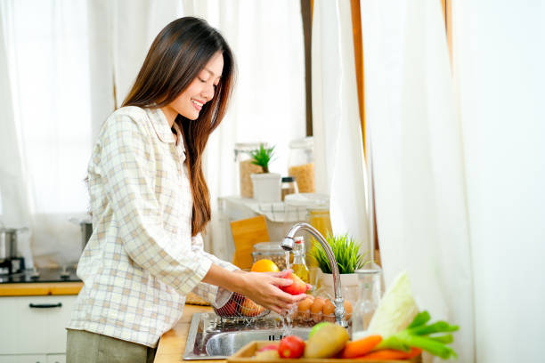 Asian beautiful teen girl is washing the apple and other fruit in the kitchen and look happy Asian beautiful teen girl is washing the apple and other fruit in the kitchen and look happy. cleaning stove domestic kitchen human hand stock pictures, royalty-free photos & images