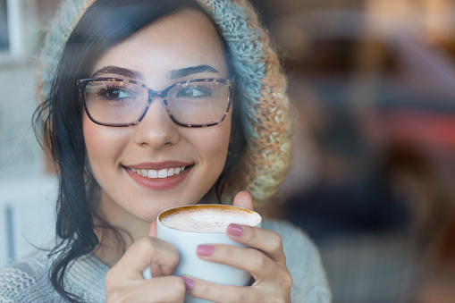 Happy young woman holding coffee mug  and dreaming while looking away