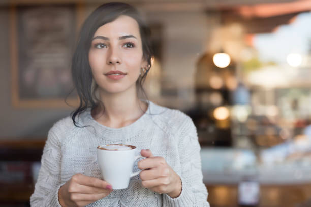 Young Woman Enjoying A Cup Of coffee At Home while looking through window