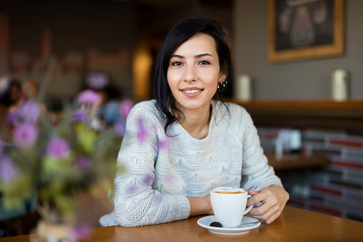 Beautiful young woman sitting at cafe table and enjoying coffee