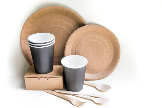 istock eco friendly disposable dishes made paper on white marble background. Draped spoons, fork, knives, plate with paper cups. recycling concept 1192621803