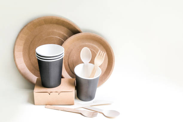istock eco friendly disposable dishes made paper on white marble background. Draped spoons, fork, knives, plate with paper cups. recycling concept 1192621827