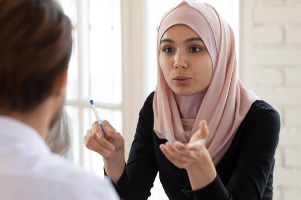 Young arabian businesswoman in hijab talking to male team leader. Concentrated serious young arabian businesswoman in hijab talking to male team leader, headshot. Focused mixed race partners discussing marketing strategy or project details together at office. arab woman stock pictures, royalty-free photos & images