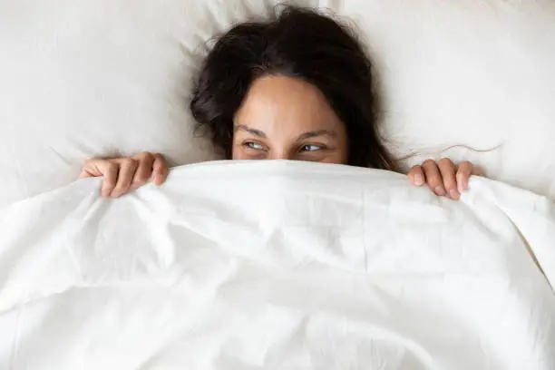 Photo of Above view playful young woman hiding face under blanket