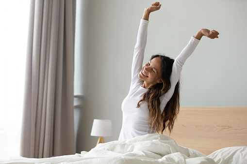 Mujer sentada en la cama estirando los músculos de los brazos después de dormir photo
