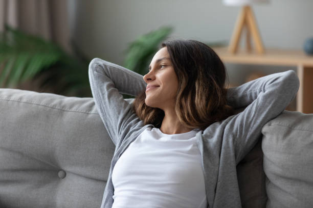 Woman put hands behind head leaned on couch resting indoors Tranquil pretty woman in casual home clothes put hands behind head leaned on couch resting in living room looking away smiling feeling serenity. Take break, keep calm, mood and free lazy time concept time pressure stock pictures, royalty-free photos & images