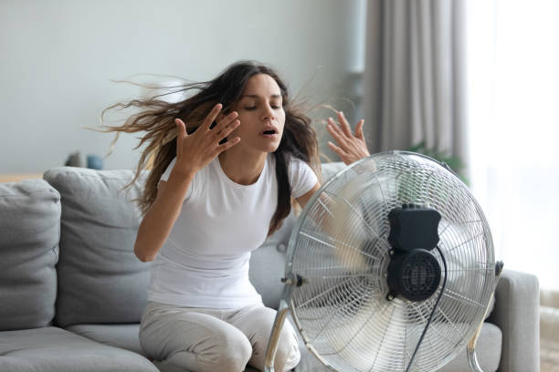 Woman turned on fan waving her hands to cool herself In living room without air-conditioner tired from summer heat young woman turned on floor ventilator waving her hands to cool herself, female sitting on couch suffers from unbearable too hot weather electric fan photos stock pictures, royalty-free photos & images