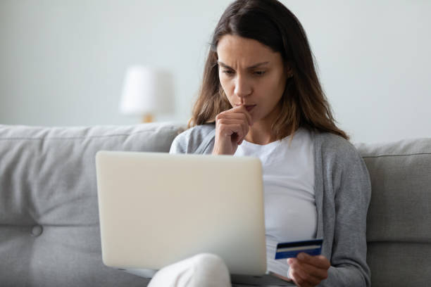 Concerned woman holding on lap computer in hand credit card
