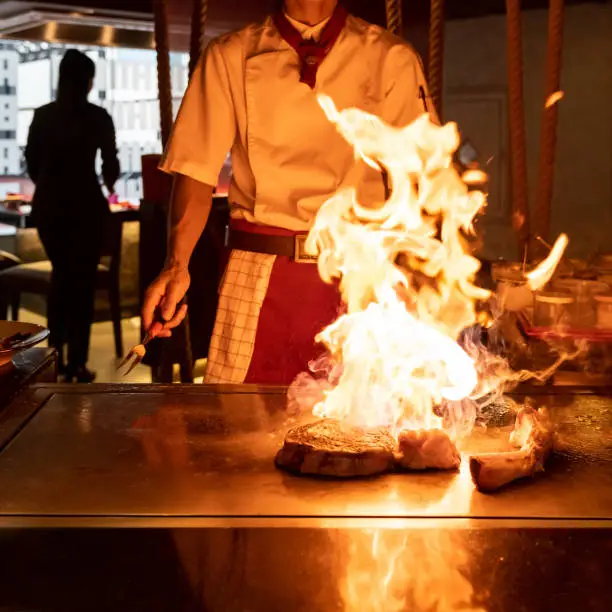 Cooking of beef teppanyaki recipe japanese grilled beef tomahawk steak on cooking pan using scraper with flame in background