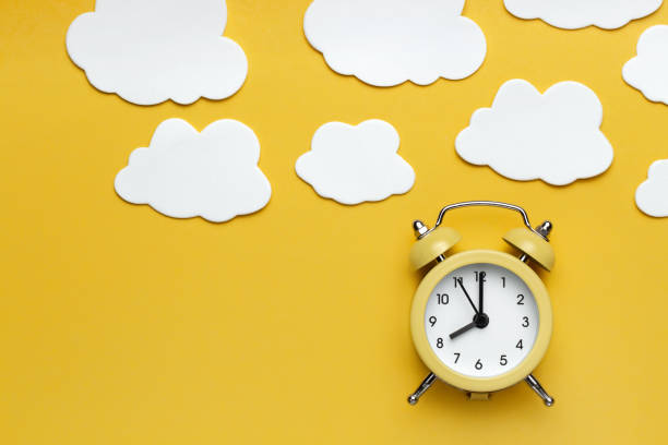 istock Yellow round alarm clock and white clouds on the yellow background. 1192635053