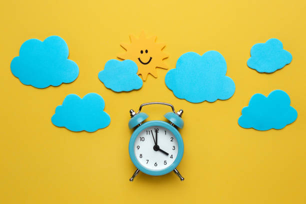 istock Blue round alarm clock, sun and clouds on the yellow background. 1192635076