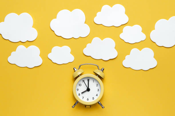 istock Yellow round alarm clock and white clouds on the yellow background. 1192635079