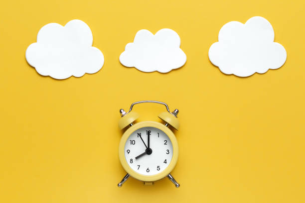 istock Yellow round alarm clock and white clouds on the yellow background. 1192635095
