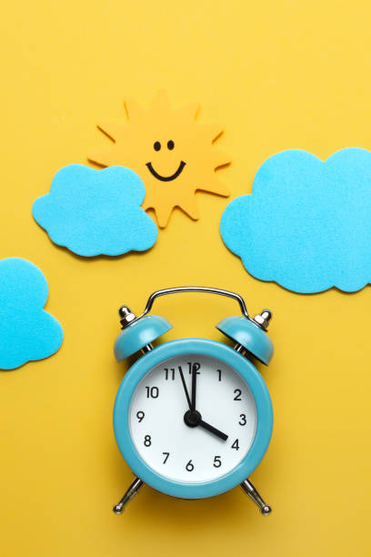 istock Blue round alarm clock, sun and clouds on the yellow background. 1192635096
