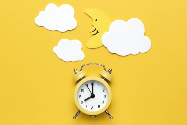 istock Yellow round alarm clock, moon and white clouds on the yellow background. 1192635099