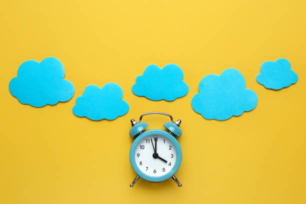istock Blue round alarm clock and clouds on the yellow background. 1192635113