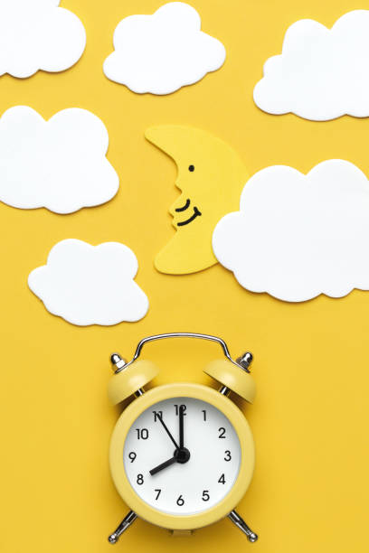 istock Yellow round alarm clock, moon and white clouds on the yellow background. 1192635120
