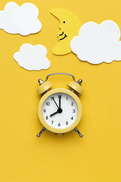 istock Yellow round alarm clock, moon and white clouds on the yellow background. 1192635125