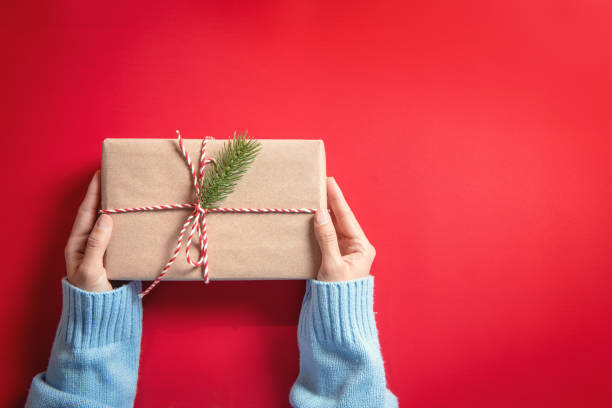 istock Woman Hands holding craft paper gift box on red background and copy space. for present Christmas and new year. 1192639996