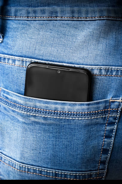 Phone in a jeans pocket Black mobile phone sticking out of the back pocket of jeans, close-up. protruding stock pictures, royalty-free photos & images