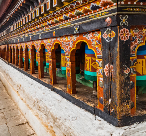 fila de ruedas de oración pintadas en bután con mantra de escritura tradicional que suena como "om mani padme hum", literalmente significa 'oh, joya en el loto'. antecedentes budistas religiosos. - bhutan himalayas wheel vibrant color fotografías e imágenes de stock
